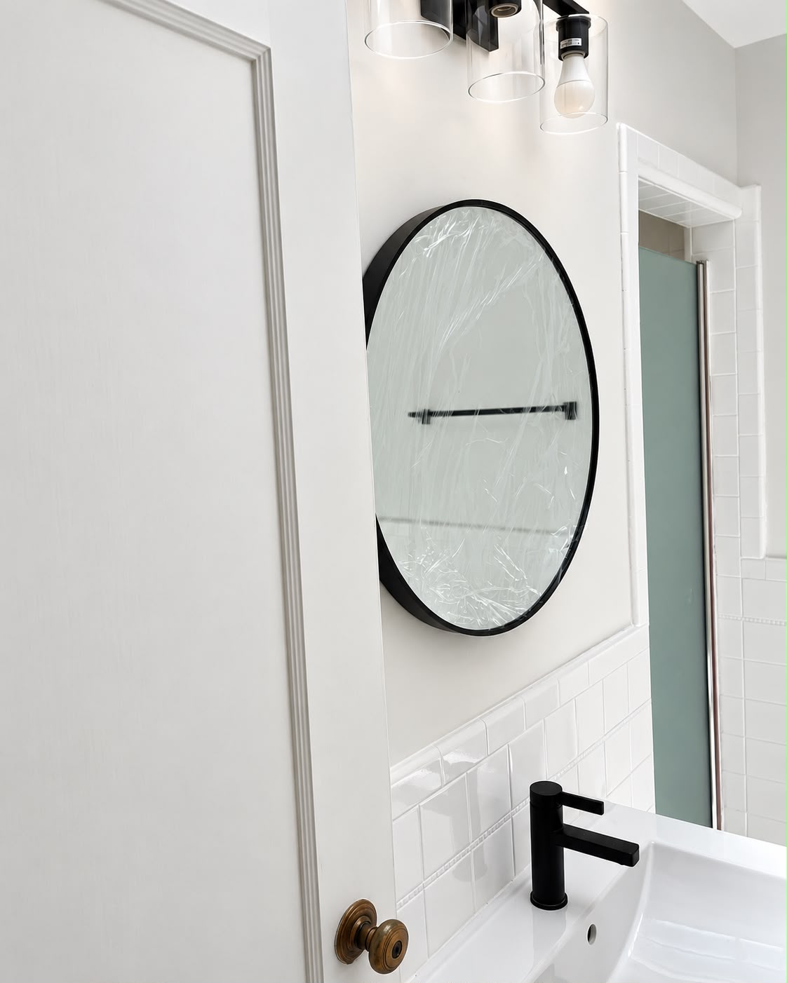 Round bathroom mirror, black faucet, and glass-shade light fixture